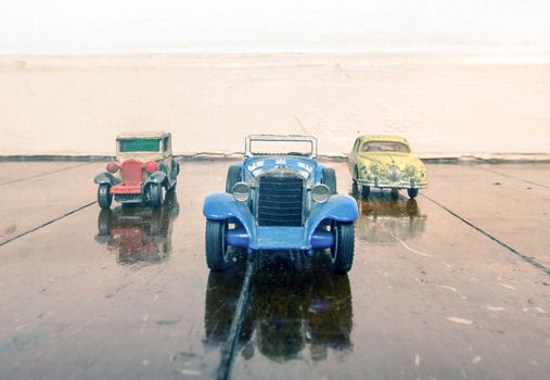 three vintage toy cars on a wooden floor with reflection
