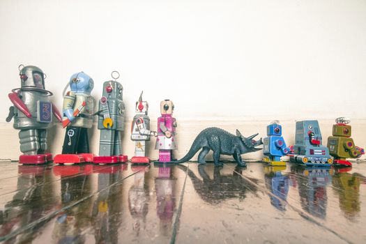 a line of retro robots with on Styracosaurus dinosaur on a wooden floor with reflection 