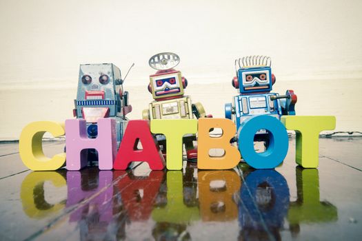 the word  CHAT BOT with wooden letters and retro toy robots  on an old wooden floor with reflection