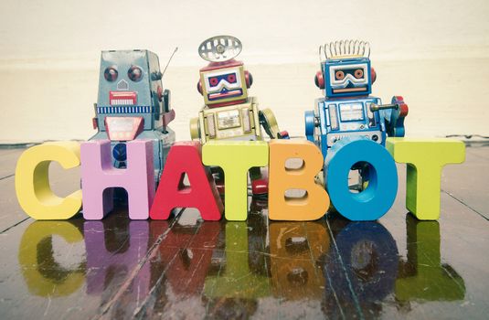 the word  CHAT BOT with wooden letters and retro toy robots  on an old wooden floor with reflection