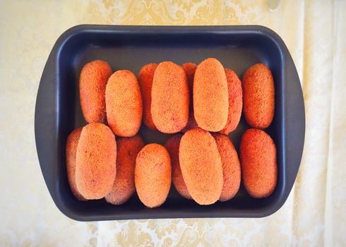 group of freshly baked arancini inside a black baking tin seen from above. Known also as Supplì