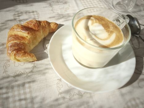 view of a foamy Cappuccino mug and a croissant