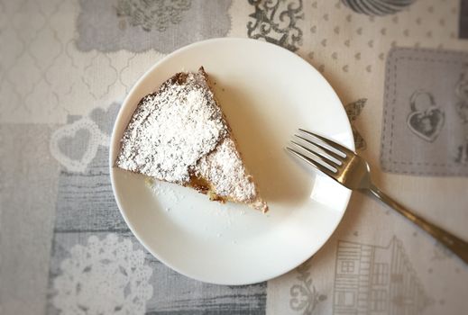Aerial view of a white plate with a slice of cake covered with icing sugar and a fork