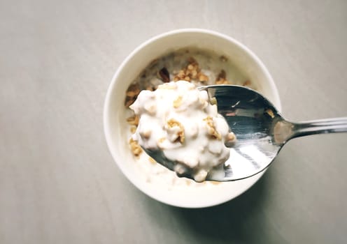 Top view of a spoon filled with yogurt and cereal with a bowl and a table set for breakfast in the background
