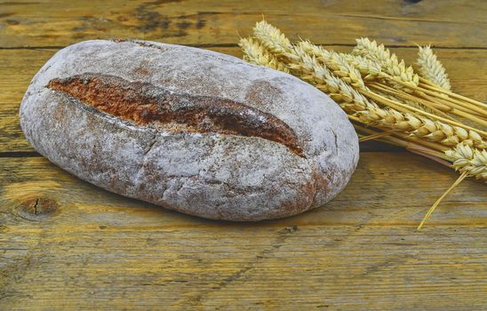 Loaf of bread and ears of grain on wood background. Rustic and rural concept. Copy space.