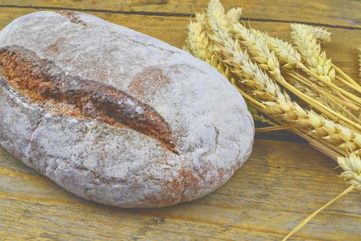 Loaf of bread and ears of grain on wood background. Rustic and rural concept. Close up.  