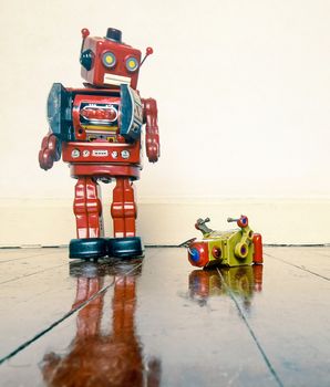 Big retro robot toy humiliates little robot on a wooden floor with reflection