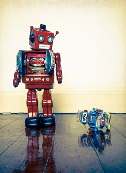 Big retro robot toy humiliates little robot on a wooden floor with reflection