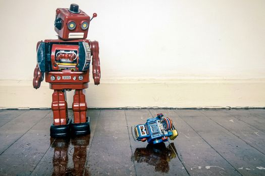 Big retro robot toy humiliates little robot on a wooden floor with reflection