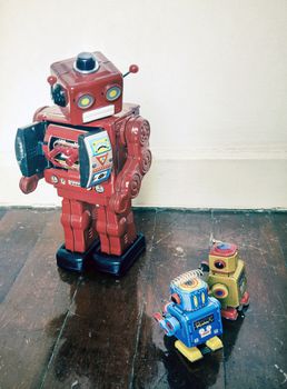 Boss robots looking down on his working robots on wooden floor with reflection