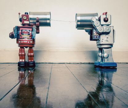 Two retro  Robots toys talking on tin can phones on an old wooden floor