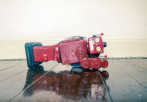 over worked retro  red robot facedown on old wooden floor with reflection