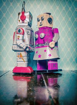 two retro robot toys in love on old wooden floor with reflection