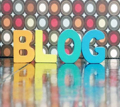 the word BLOG  with color wooden letters on an old wooden floor with reflection 