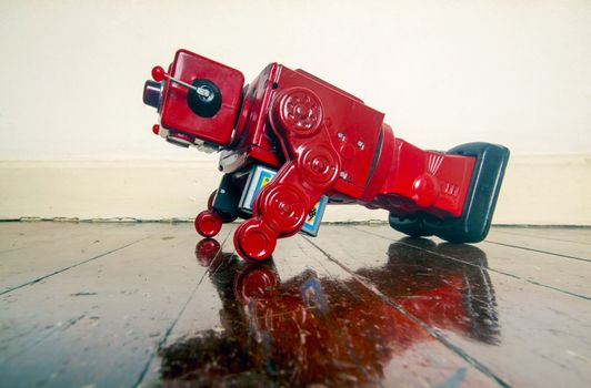 red retro robot toy doing push ups on an old wooden floor with reflection 