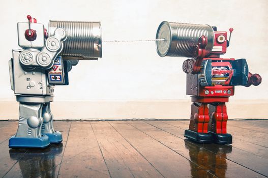 Two retro  Robots toys talking on tin can phones on an old wooden floor 