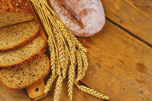 Loafs of bread, slices of bread and ears of grain on wood background. Rustic and rural concept. Copy space.