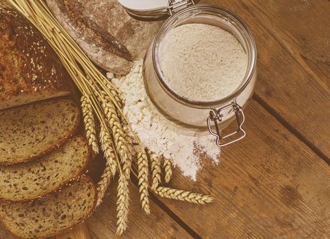 Loafs of bread, slices of bread, wheat flour and ears of grain on wood background. Rustic and rural concept. Close up. Flat lay. Copy space.