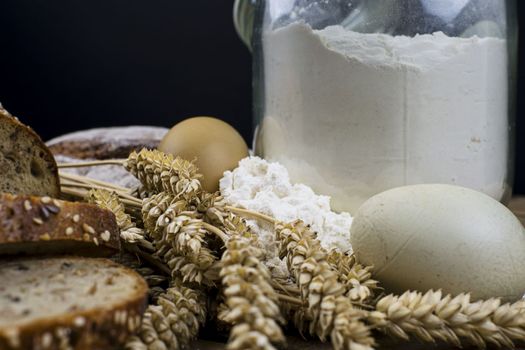 Loafs of bread, slices of bread, wheat flour, eggs and ears of grain on wood background. Rustic and rural concept. Close up. Copy space.