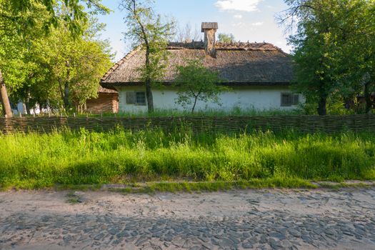 Stone road passing near the old Ukrainian house with a wicker fence and a green garden