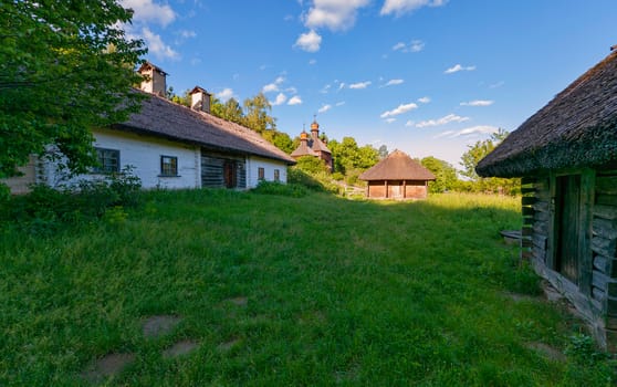 Wooden barn in a village on the background of an old church under a blue sky dome