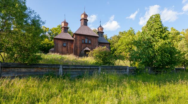 An old wooden church with three shining domes overgrown with tall grass. As in the film Viy