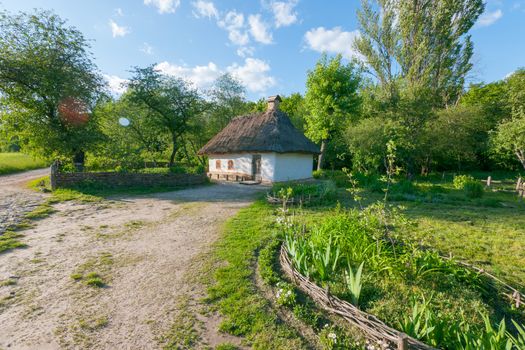 old Ukrainian house of a mud hut in a village on a green lawn in a blue cloudy sky