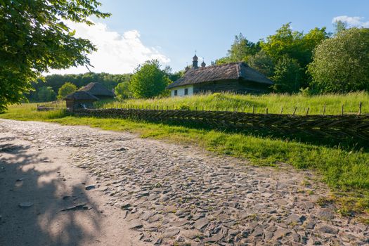 Old houses and a church on a green meadow are protected by a wicker fence