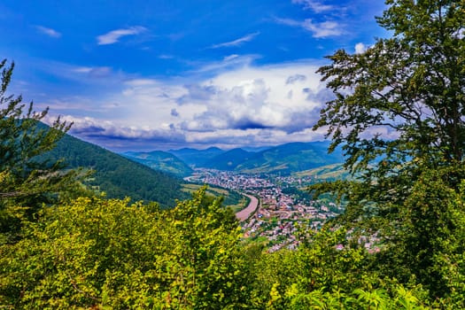 Magnificent landscape of the mountain valley with the city lying down. With emerald green peaks and thick white dense clouds above them.