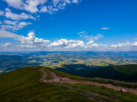 dirt road on the ridge of a tall mountain covered with green dense grass rising to a blue sky with clouds