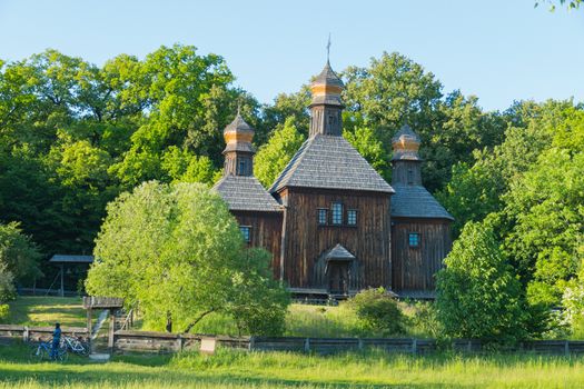 An ancient wooden church with three domes in the shade of lush green trees