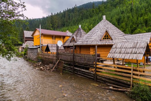 wooden Hutsul manor on the steep bank of the river at the foot of the mountains in the Carpathians
