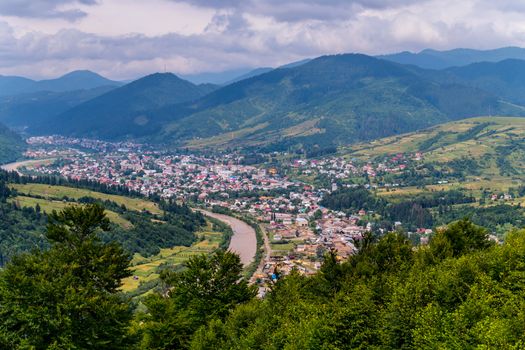 A panorama of the city along the river in the valleys at the foot of the mountain ridge covered with fires