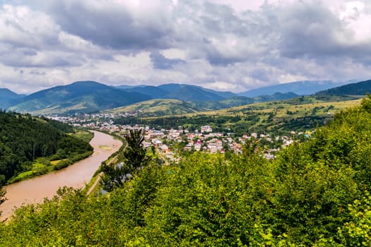A chic mountain landscape against a cloudy sky and a green forest and a small town in the valley
