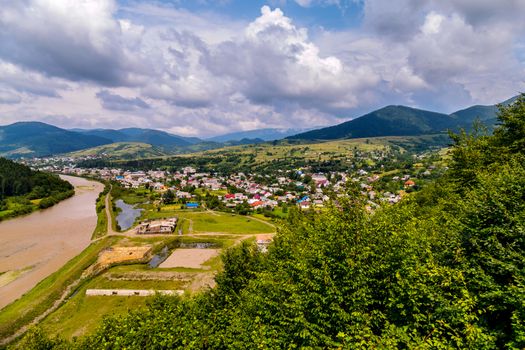 colored roofs of houses of the city stretching along the brown river between the Carpathian slopes