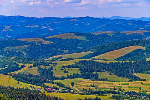 picturesque landscape of wooded hills with grassy bumps and squares of agricultural land