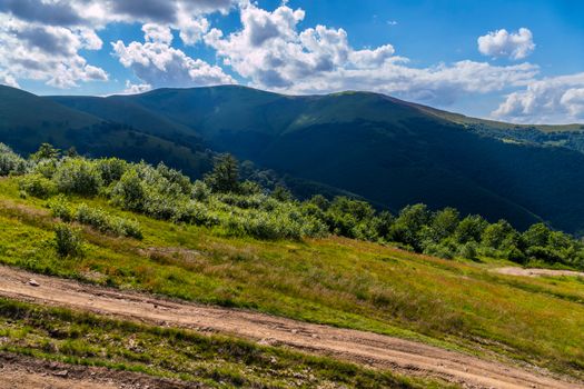light dust of a dirt road running along green bushes and mountain peaks