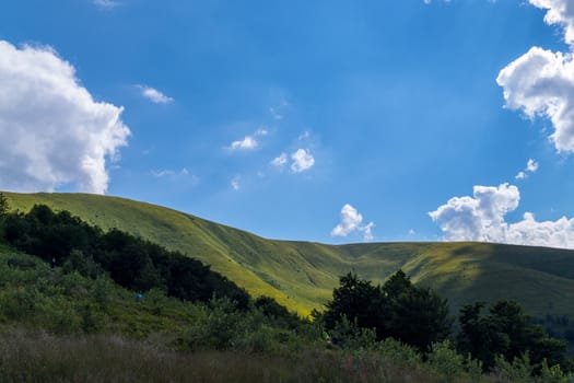 The green mountain valley is flooded with sunlight. The blue clear sky