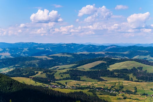 village in a mountain valley, green trees and blue sky with clouds