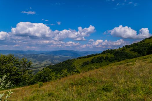 grassy sloping descent, overlooking the countryside of the mountains and hills under the blue sky
