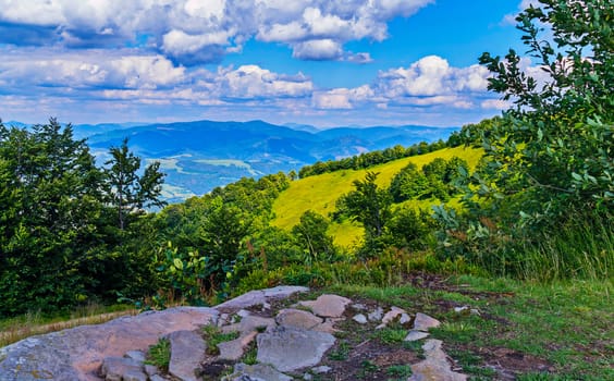 A beautiful view from the glade with stones to the picturesque mountain slopes with the haze of the blue sky in the midday heat.