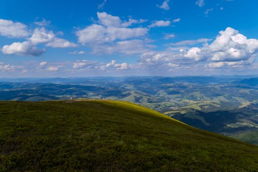 Tourists in the distance on the edge of the green platform admire the beauty of the nature of the mountains and valleys stretching far to the horizon line.