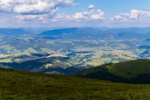 Green fields, deciduous forests and a small rural village at the foot of the summit of a huge mountain