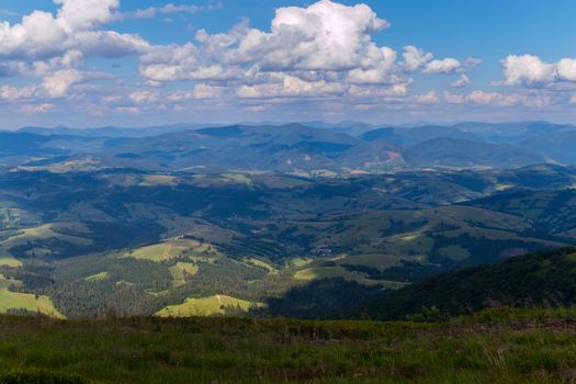 View from the top of the mountain to the forest glades, fields and village in the bright summer sun