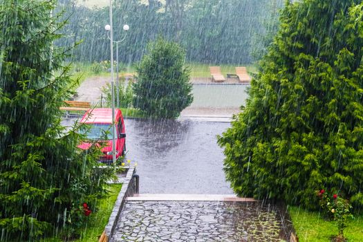 Drops of very heavy rainfall fall on asphalt and trees near the hotel complex