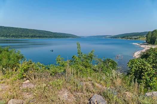 A fisherman on a boat in the middle of a beautiful endless blue lake against the background of green mountains