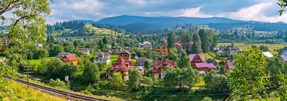 beautiful panorama of the Transcarpathian village with elite houses near the railway on the background of the blue mountains