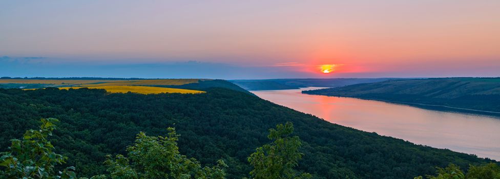 a masterpiece panorama of the setting sun on the river green of the tops of trees and gold of wheat fields