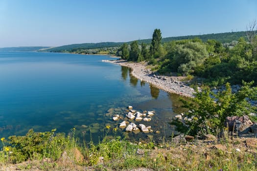 Holidaymakers on the stone shore of a huge blue clear lake against the background of green mountain ranges
