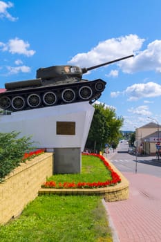 Monument with a tank against a beautiful green flowerbed with red flowers